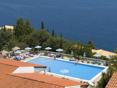 Vue d'une piscine avec parasols et transats, mer en arrière-plan.
