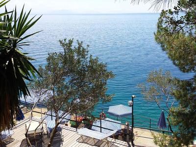 Terrasse mit Sitzgelegenheiten und Blick auf das Meer, umgeben von Bäumen und Pflanzen.