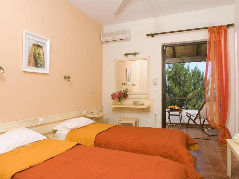 Hotelkamer met twee eenpersoonsbedden, oranje dekens en toegang tot balkon met stoelen.