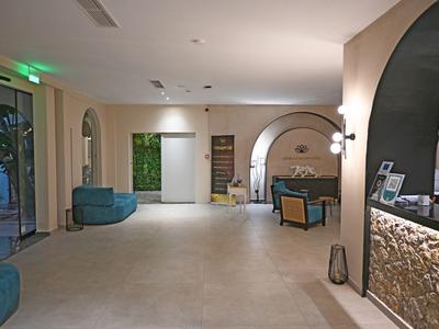 Jasne lobby hotelowe z fotelami, zieloną ścianą i nowoczesnym recepcją.