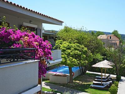 Hotelbalkon met bloeiende planten, terras en tuin met ligstoelen en parasol.