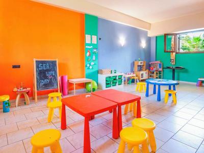 Kleurrijke speelkamer voor kinderen met kleine tafels en krukjes in een lichte, vrolijke ruimte.