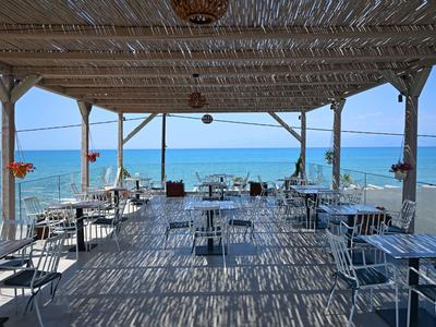 Open strandbar met houten dak en uitzicht op de blauwe zee, ingericht met tafels en stoelen.