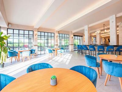 Lichte hotel eetruimte met grote ramen, blauwe stoelen en houten tafels.