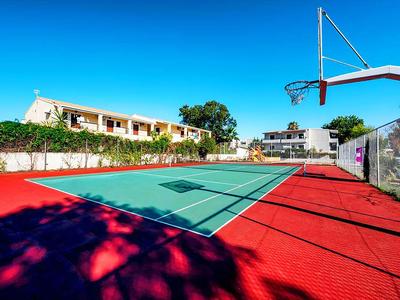 Leeg tennisveld met rode ondergrond en blauwe lucht, omgeven door hotelgebouwen.