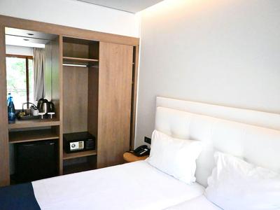 Lichte hotelkamer met tweepersoonsbed, kledingkast en bureau.
