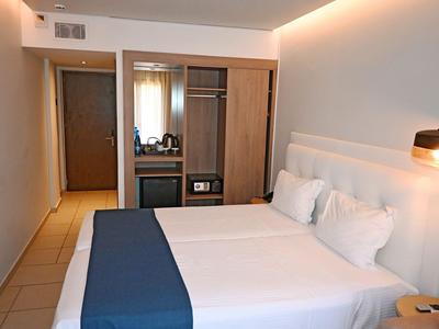 Modern hotelkamer met groot tweepersoonsbed, lichte muren en open kast.