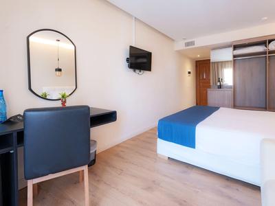 Modern hotelkamer met tweepersoonsbed, bureau, stoel en aan de muur gemonteerde tv.