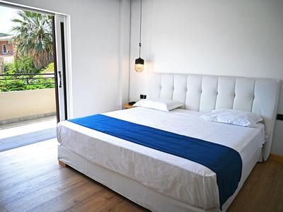 Lichte hotelkamer met tweepersoonsbed, blauw bedlaken, houten vloer en balkon met groene uitzicht.