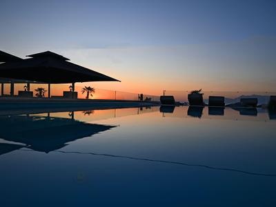Een infinity-zwembad bij zonsondergang met ligstoelen en een overdekt gedeelte op de achtergrond.
