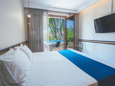 Modern hotelkamer met groot bed, balkon en uitzicht op groene bomen.
