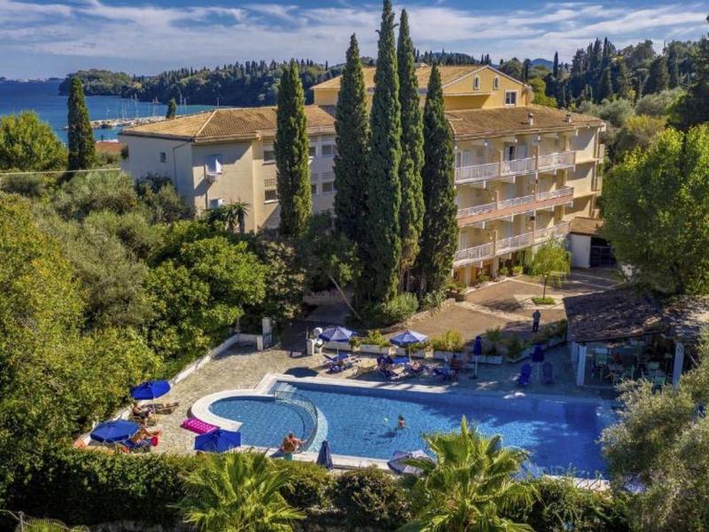 Complejo hotelero con piscina rodeada de árboles y vista al mar al fondo.