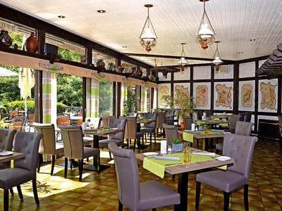 Helles Restaurant mit Holzbalkendecke, stilvollen Stühlen und Tischen, großen Fenstern und dekorativen Wandbildern.