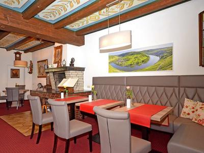 Gemütliches Restaurant mit Holzbalkendecke, Kamingrill, grauen Stühlen und rot gedeckten Tischen.