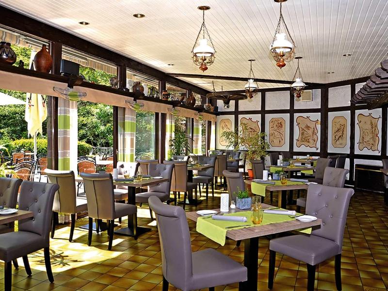 Salle à manger confortable avec tables dressées et chaises, entourée de grandes fenêtres donnant sur un jardin