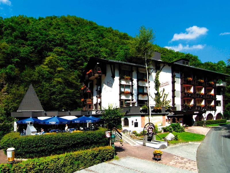 Bâtiment d'hôtel avec chambres balcon devant une colline boisée et parasols bleus