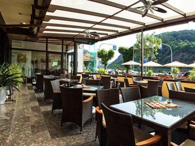 Überdachte Terrasse mit braunen Stühlen, Tischen, Pflanzen und Aussicht auf grüne Hügel.