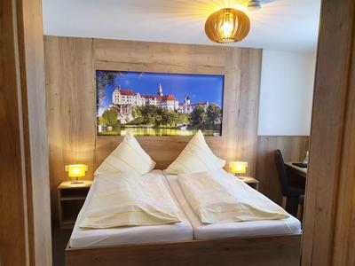 Gemütliches Doppelbett mit weißen Kissen und Decken vor einer Holzpaneelwand mit einem Foto eines Schlosses.