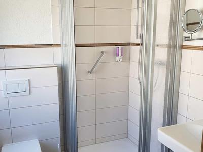 Kleines Badezimmer mit Duschkabine, Toilette und Waschbecken in hellen Fliesen.