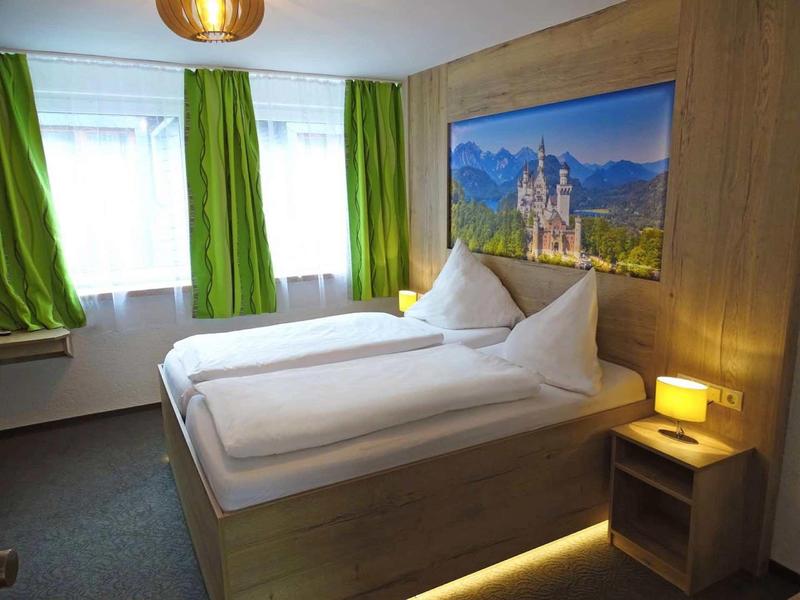 Schlafzimmer mit Doppelbett, grünen Vorhängen und einem Bild einer Burg an der Holzwand.