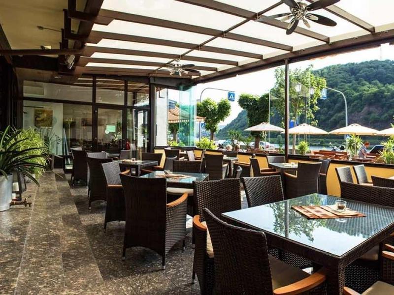 Überdachte Terrasse mit braunen Stühlen, Tischen, Pflanzen und Aussicht auf grüne Hügel.