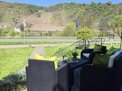 Sitzbereich im Freien mit schwarzen Möbeln und gelben Kissen vor grüner Landschaft und Hügeln.