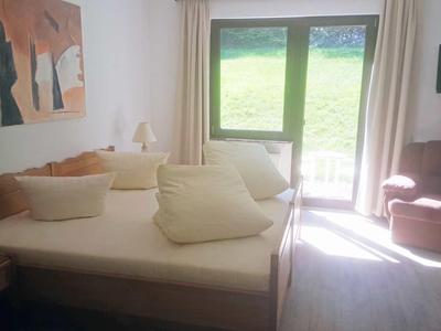 Hell eingerichtetes Wohnzimmer mit Sofa, Sessel, Fernseher und Blick auf eine grüne Wiese.