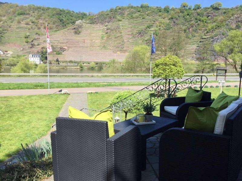 Sitzbereich mit schwarzen Polstermöbeln und bunten Kissen vor grünem Hügel und blassem Himmel.