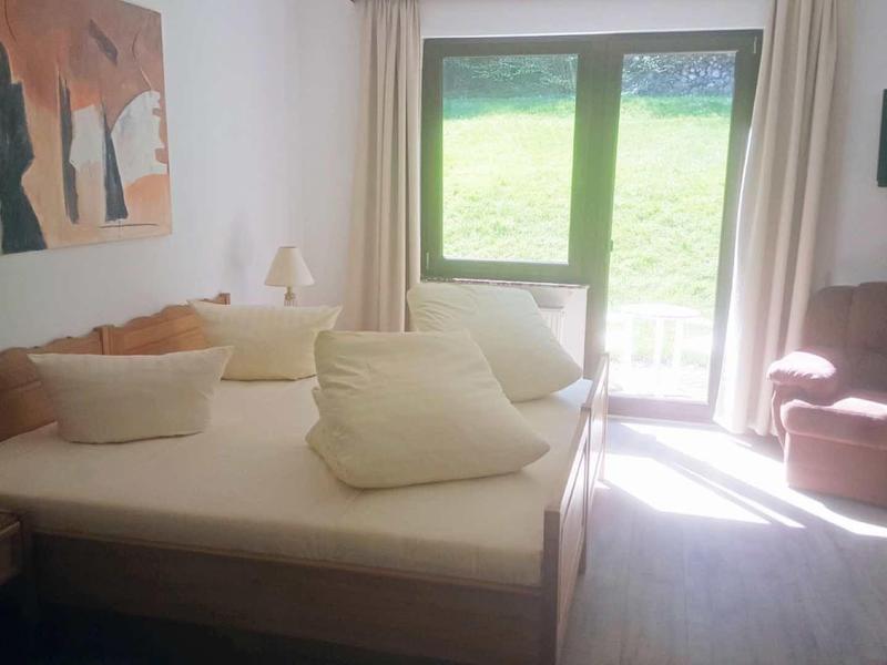 Helles Schlafzimmer mit großem Bett, zwei Sesseln, Holzfußboden und Fenster mit Blick ins Grüne.