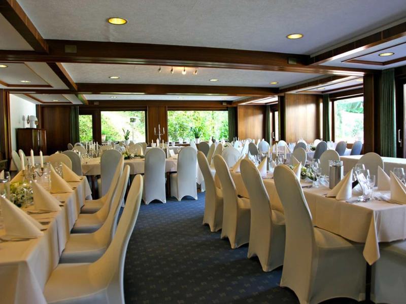 Eleganter Speisesaal mit weißen Tischdecken, Stuhlbezügen und gedeckten Tafeln unter Holzbalken.