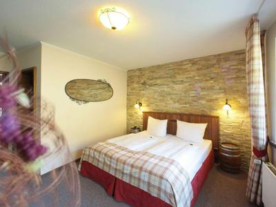 Gemütliches Schlafzimmer mit großem Bett, Steinwand, warmem Licht und Vorhängen am Fenster.