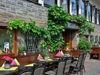 Außenterrasse eines Cafés mit gedeckten Tischen, grünen Pflanzen und Blumendekoration am Gebäude.