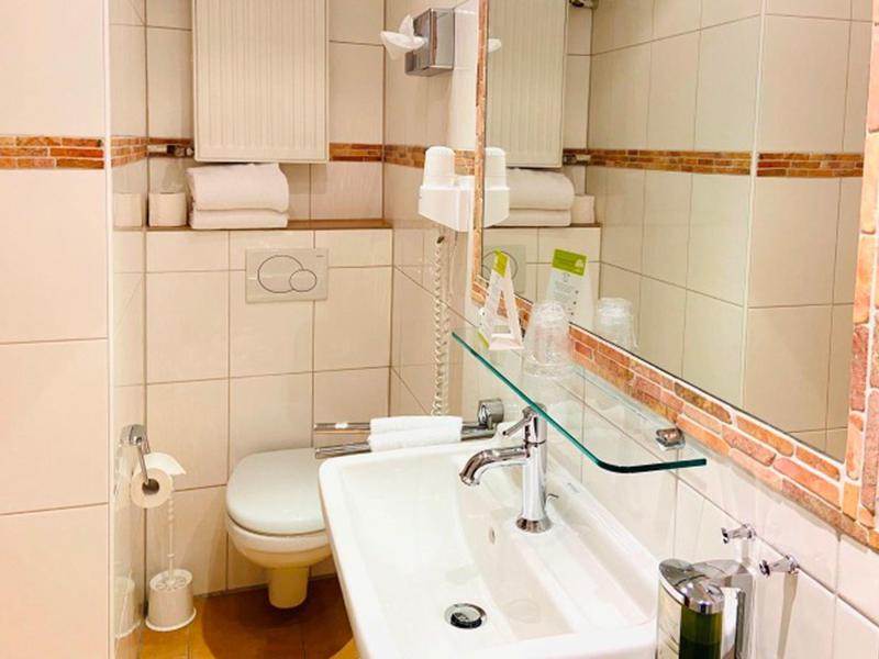 Kleines weiß gefliestes Badezimmer mit Waschbecken, Toilette, Spiegel und Handtüchern.