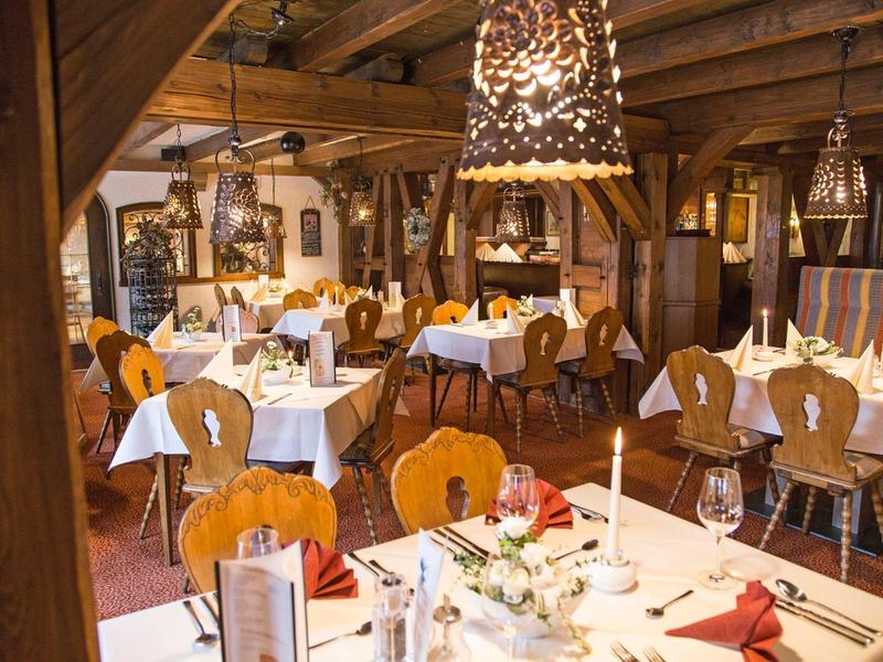 Rustikales Restaurant mit Holzmöbeln, weiß gedeckten Tischen und warmem Beleuchtungskonzept.