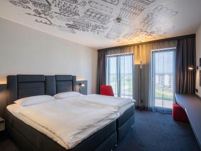 Modernes Schlafzimmer mit Doppelbett, grauem Teppich, großen Fenstern und weißer Decke mit schwarzem Muster.