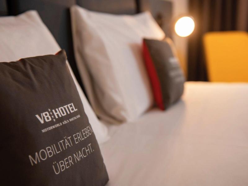 Nahaufnahme eines Bettes mit dunklem Kissen, das weißen Text und Logo trägt, und unscharfen Kissen im Hintergrund.