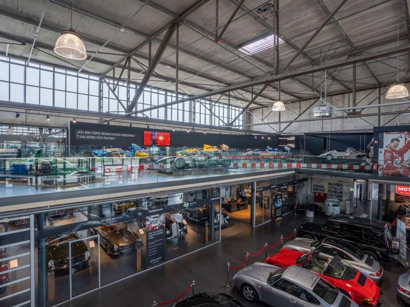 Moderne Autowerkstatt mit Glaswänden, mehreren Autos und hoher Decke mit Stahlträgern.