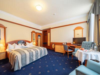 Helles Hotelzimmer mit Doppelbett, Schreibtisch, Sessel und einem Tisch mit Stühlen.