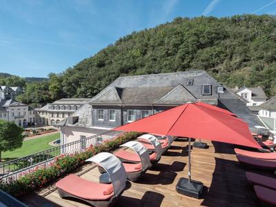 Ein Hotel-Dachterrasse mit Liegen und roten Sonnenschirmen, umgeben von grünen Hügeln.