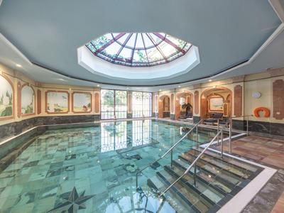 Hell beleuchteter Schwimmbadraum mit Kuppelgewölbe und kunstvollen Wandmalereien.