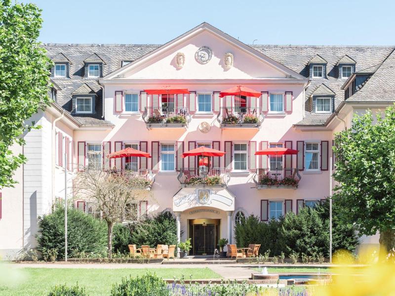 Historisches Hotelgebäude mit rosa Fassade und roten Sonnenschirmen auf den Balkonen