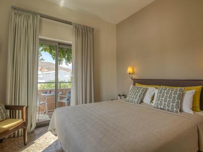 Chambre d'hôtel avec lit double, fauteuil et balcon donnant sur un paysage verdoyant.