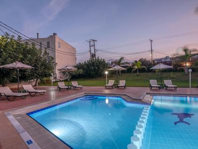 Piscine extérieure éclairée avec chaises longues et parasols dans le jardin de l'hôtel au crépuscule.