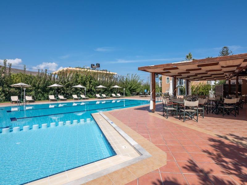 Grande piscine extérieure avec parasols et terrasse couverte sous un ciel clair.