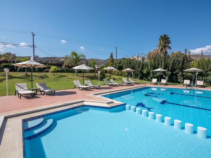 Piscine bleue claire avec transats et parasols sur pelouse verte sous ciel bleu.