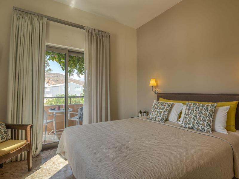 Chambre d'hôtel avec lit double, fauteuil et balcon donnant sur un paysage verdoyant.