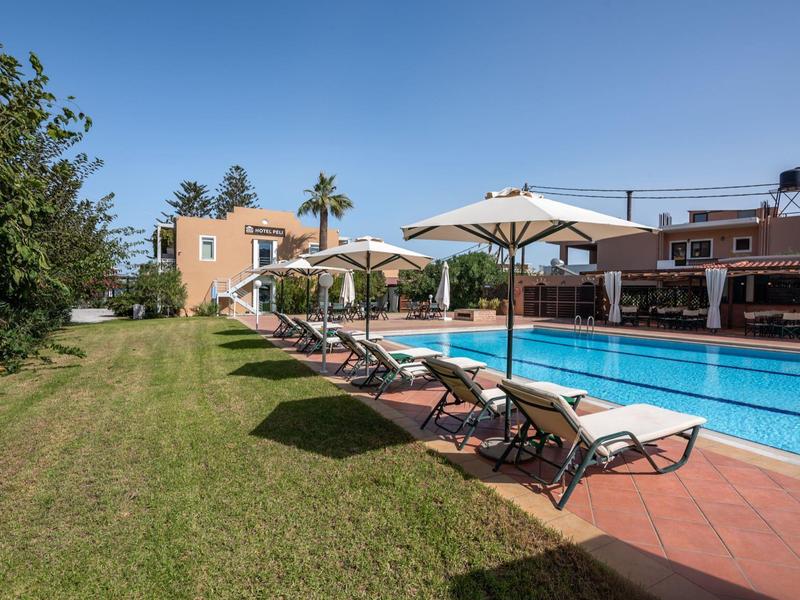 Zone de piscine avec chaises longues et parasols à côté d'un bâtiment hôtelier sous un ciel bleu.