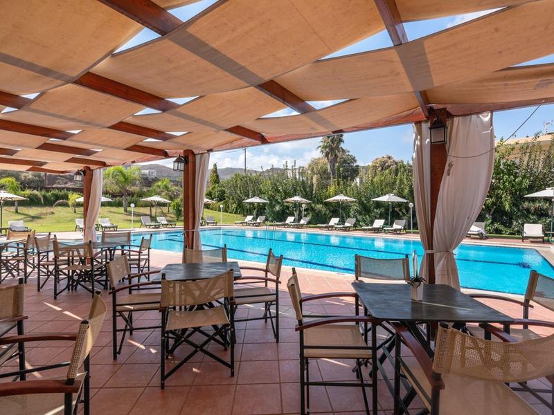 Terrasse couverte avec chaises et tables à côté d'une piscine dans un hôtel ensoleillé.