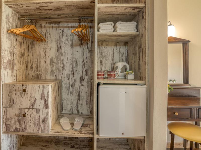 Armoire ouverte en bois avec chaussures, serviettes et mini-réfrigérateur.