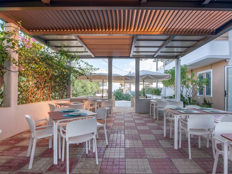 Espace café extérieur couvert avec tables et chaises blanches donnant sur le jardin.